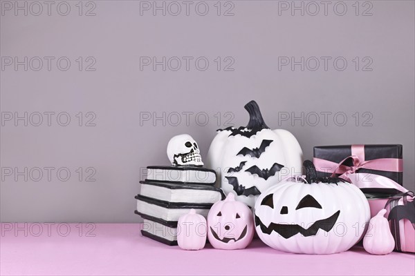 Pink and white Halloween decor with black and white pumpkins, spell books and spiders on gray background with copy space