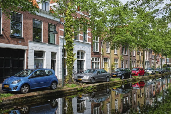 Delft, Netherlands, May 12, 2017: Cars and bicycles parked on canal embankment in street of Delft with reflection. Delft, Netherlands