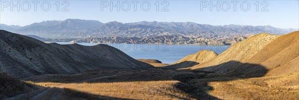 Panorama, blue Toktogul reservoir between dry mountain landscape, hilly mountains in the evening light, Jalalabad region, Kyrgyzstan, Asia