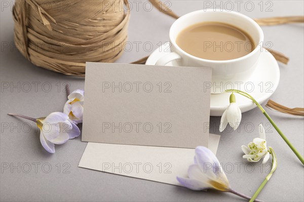 Gray paper business card mockup with spring snowdrop crocus and galanthus flowers and cup of coffee on gray background. Blank, business card, side view, copy space, still life. spring concept