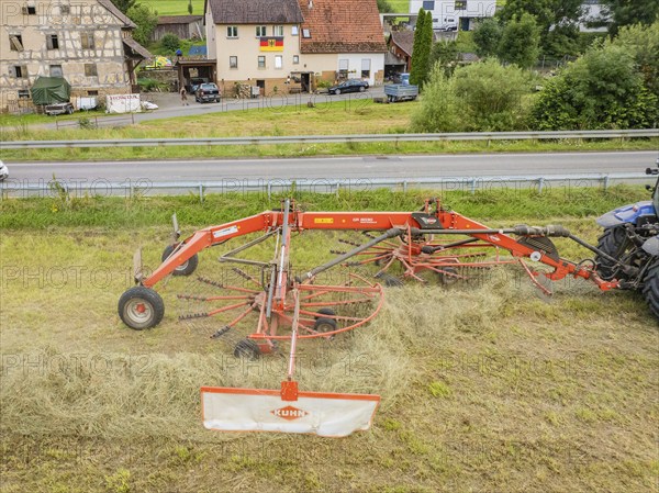 Close-up of a haymaking machine in a field, with a building and a road in the background, Dachtel. Black Forest, Germany, Europe