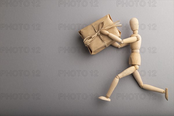 Wooden mannequin holding a gift box on gray pastel background. copy space, isolated, delivery concept