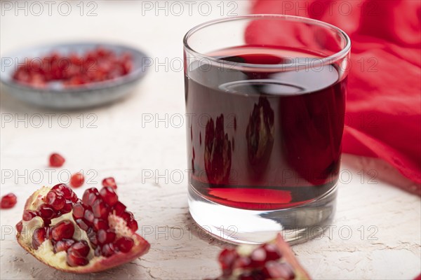 Glass of pomegranate juice on a white concrete background with red textile. Side view, close up, selective focus