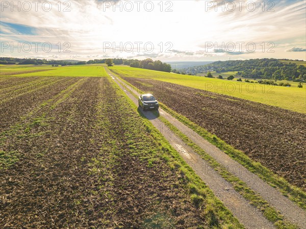A car drives along a rural road, surrounded by expansive fields under bright daylight, car sharing, VW ID5, Calw, Black Forest, Germany, Europe