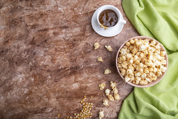 Popcorn with caramel in ceramic bowl on brown concrete background and green textile. Top view, flat lay, copy space