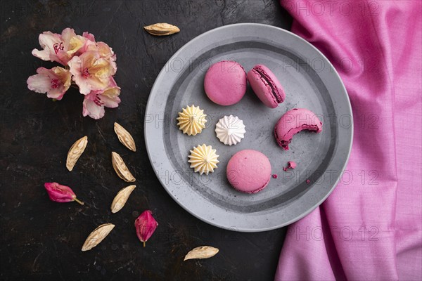 Purple macarons or macaroons cakes with cup of coffee on a black concrete background and pink textile. Top view, flat lay, close up