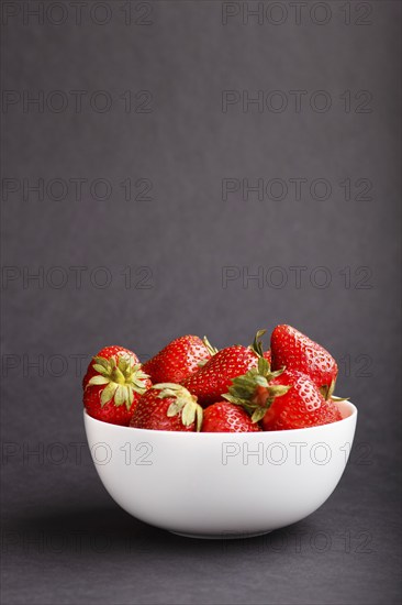 Fresh red strawberry in white bowl on black background. side view, copy space