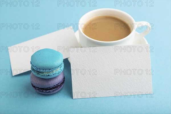 White paper business card mockup with blue and violet macaroons and cup of coffee on blue pastel background. Blank, side view, copy space, still life, close up. morning, breakfast concept