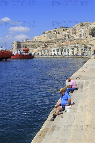 Men fishing historic waterfront buildings on quayside, Valletta, Malta, Europe