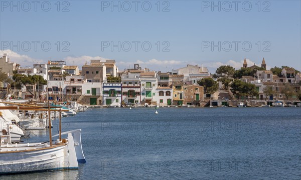 Quiet harbour with boats in the foreground and colourful buildings along the coast under a blue sky, Portocolom, Majorca, Balearic Islands, Spain, Europe