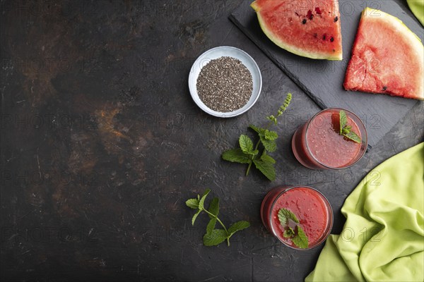 Watermelon juice with chia seeds and mint in glass on a black concrete background with green textile. Healthy drink concept. Top view, copy space, flat lay
