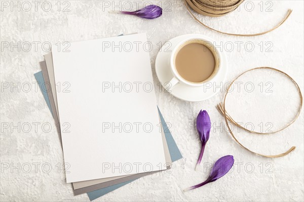 White paper sheet mockup with spring snowdrop crocus flowers and cup of coffee on gray concrete background. Blank, business card, top view, flat lay, copy space, still life. spring concept