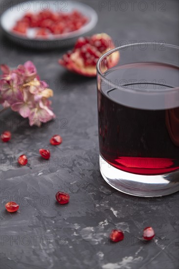 Glass of pomegranate juice on a black concrete background with red textile. Side view, close up, selective focus