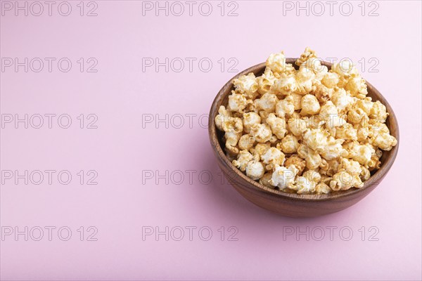 Popcorn with caramel in wooden bowl on a pastel pink background. Side view, copy space