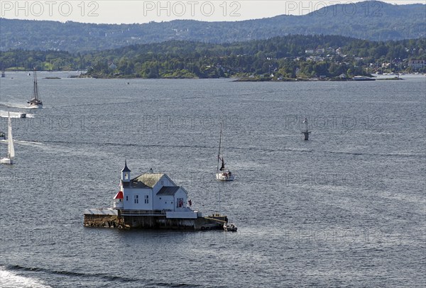 Small lighthouse on an island in the water, surrounded by boats and hills in the distance, Dyna Fyr, Oslofjord, capital city, Oslo, Norway, Europe