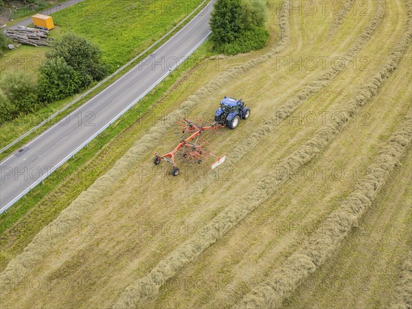 Aerial view of a tractor with hay machine in a field next to a country road, Dachtel. Black Forest, Germany, Europe
