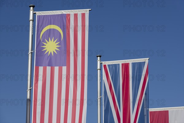 Several flags of different countries fly side by side under a clear blue sky, Malaysian flag, English flag