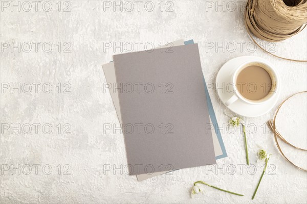 Gray paper sheet mockup with spring snowdrop galanthus flowers and cup of coffee on gray concrete background. Blank, business card, top view, flat lay, copy space, still life. spring concept
