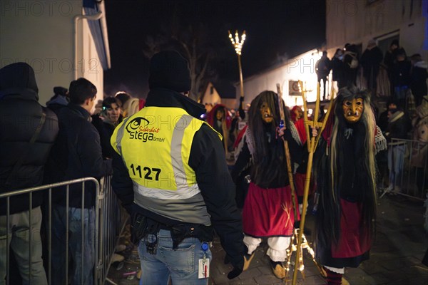 Security employee observes group of masked persons at a night event, carnival, Schellbronn night parade, Schellbronn, Germany, Europe