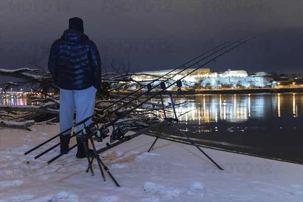 Night Fishing Fisherman in Winter night. Night Fishing, Winter fishing. Carp Rods, Night reflection. City lights