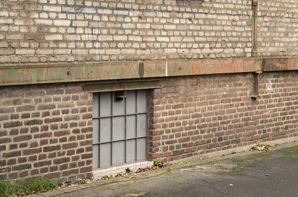 Frosted glass basement window illuminating a weathered industrial brick wall building, showcasing urban decay and architectural texture