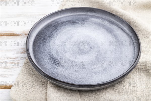 Empty gray ceramic plate on white wooden background and linen textile. Side view, close up
