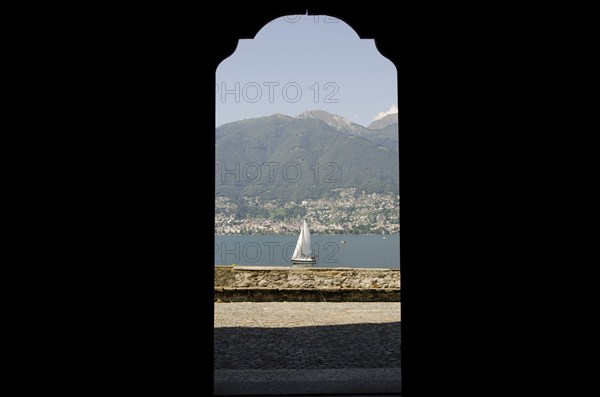 Looking at a Sailing Boat Through an Open Door on Lake Maggiore with Mountain in a Sunny Summer Day in Ticino, Switzerland, Europe