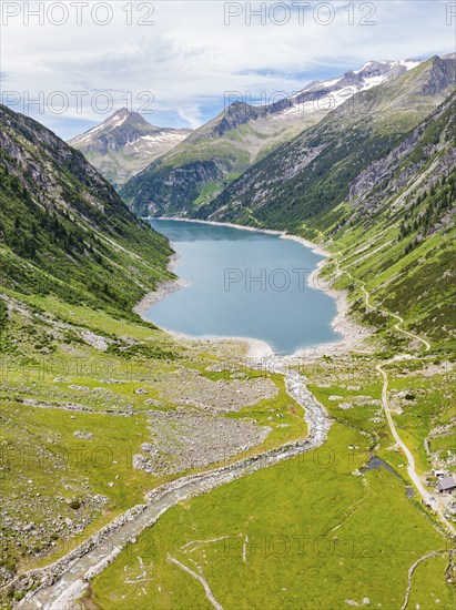 An alpine lake surrounded by green meadows and mountains, with a river and a hiking trail under a cloudy sky, Klein Tibet, Zillertal, Austria, Europe