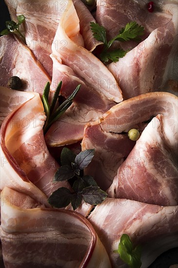 Raw bacon, sliced, with micro greenery and spices, on a black background, close-up