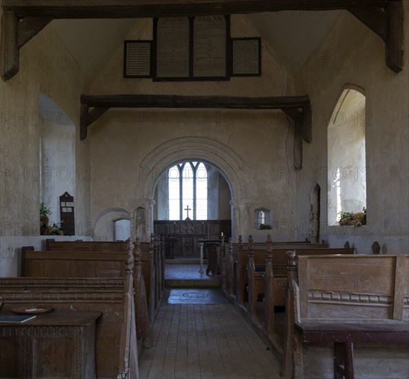 Norman chancel arch and wooden pews inside church of Saint John the Baptist, Wantisden, Suffolk, England, UK