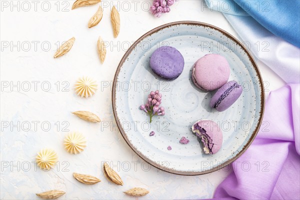 Purple macarons or macaroons cakes with cup of coffee on a white concrete background and magenta-blue textile. Top view, flat lay, close up