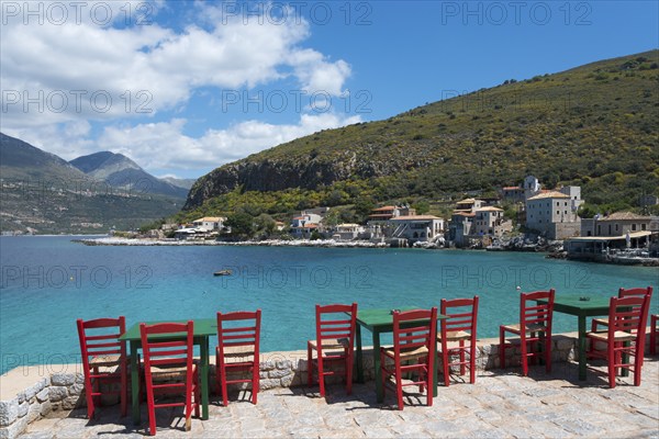 Empty red chairs on a sunny day on the shore of a calm blue sea, Limeni, Areopoli, Laconia, Peloponnese, Greece, Europe