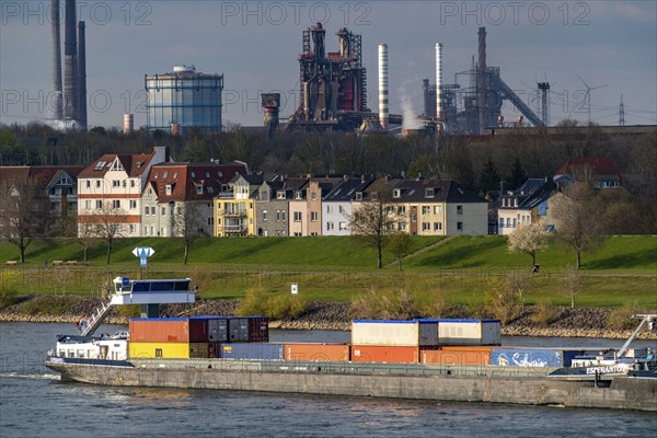 Cargo ships on the Rhine near Duisburg-Laar, houses on Deichstrasse, industrial backdrop of the ThyssenKrupp Steel steelworks in Bruckhausen, North Rhine-Westphalia, Germany, Europe