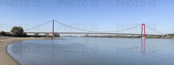 Panorama view from the left bank of the Rhine, western bank of the Rhine, of an earth-anchored suspension bridge with two abutments and red steel piers nicknamed the Golden Gate of the Lower Rhine over the River Rhine, with a total length of 1228 metres the longest suspension bridge in Germany, Emmerich, North Rhine-Westphalia, Germany, Europe
