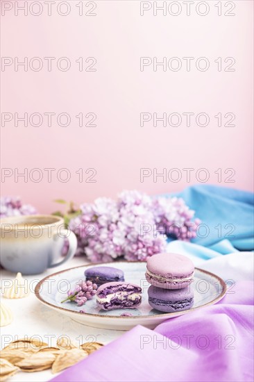 Purple macarons or macaroons cakes with cup of coffee on a white and pink background and magenta-blue textile. Side view, copy space, selective focus