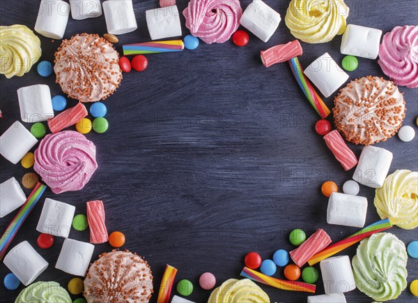 Colorful frame of multicolored candies on black wooden background. Circle copy space, top view, flat lay