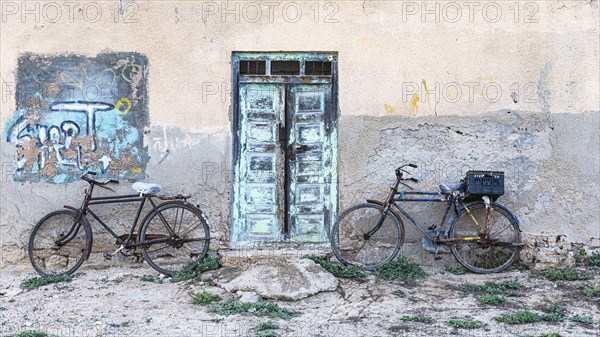 Old bicycles leaning against a house wall with an old wooden door, on the beach of Salalah, Dhofar Province, Arabian Peninsula, Sultanate of Oman