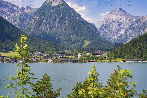 Lake surrounded by green mountains with a small cluster of houses in the sunlight, Achernsee, Austria, Germany, Europe