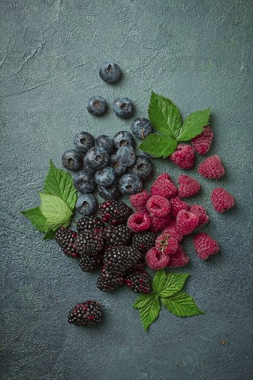 A mix of ripe berries, with leaves scattered on the table, raspberries, blackberries, blueberries, food background