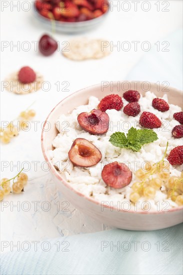 Rice flakes porridge with milk and strawberry in ceramic bowl on white concrete background and blue linen textile. Side view, close up, selective focus