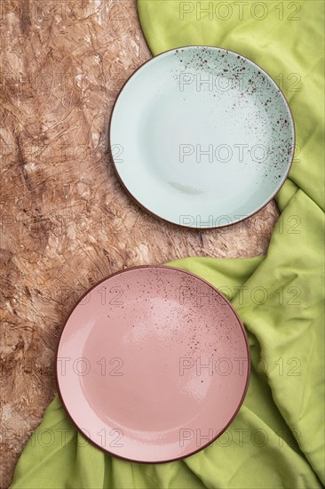 Two empty blue and pink plates on brown concrete background and green textile. Top view, close up, flat lay