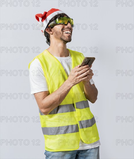 Happy Engineer in christmas hat using cell phone isolated. Smiling engineer in christmas hat using cell phone. Concept of engineer with christmas hat laughing while using cell phone at christmas
