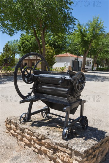 Historische Metallmaschine mit großen Rädern auf einem steinigen Untergrund im Freien, umgeben von Bäumen, antike Wäschemangel, Eremitage und Museum Virgen de las Viñas, Heiligtum Unserer Lieben Frau, der Heiligen Jungfrau der Reben, Tomelloso, Ciudad Real, Kastilien-La Mancha, Spanien