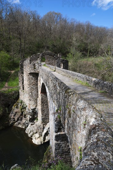 Historische Steinbrücke, die über einen Fluss führt, umgeben von Wald und Ruinenresten unter einem blauen Himmel, Brücke des Teufels, Pont de Diable, romanische Steinbrücke, Fluss Ariège, Montoulieu, Ariege, Frankreich