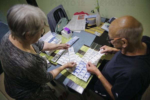 Symbolic photo on the subject of taking medication in old age. Two senior citizens sort various tablets into pill boxes at home to take for the next 16 days. Berlin, 27.07.2024