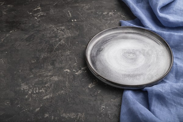 Empty gray ceramic plate on black concrete background and blue linen textile. Side view, copy space, close up