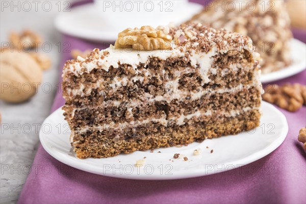 Homemade cake with milk cream and walnuts with cup of coffee on a gray concrete background and purple textile. side view, close up, selective focus