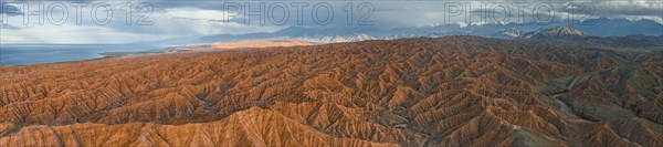 Panorama, landscape of eroded hills, badlands at sunset, behind mountain peaks of the Tian Shan Mountains and Issyk Kul Lake, aerial view, Canyon of the Forgotten Rivers, Issyk Kul, Kyrgyzstan, Asia