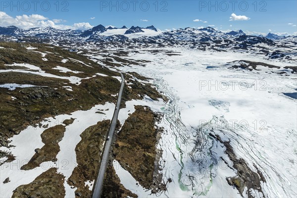 Aerial view of mountain crossing Sognefjellsvegen, along frozen lake Prestesteinsvatnet, view towards glaciers, Sognefjell, Norway, Europe