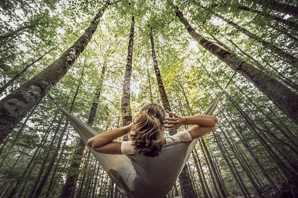A woman lies in a hammock and looks up at the wooded sky